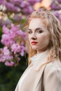 Portrait of blonde woman with red lips and haughty expression near blossom tree. Successful business woman outdoors. Vertical