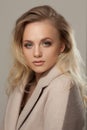 Portrait of a blonde woman wearing beige coat, looking over shoulder.