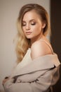 Portrait of a blonde woman wearing beige coat, looking over shoulder.