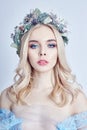 Portrait of a blonde woman with a wreath on her head and a blue delicate light transparent dress. Big blue eyes and beautiful skin