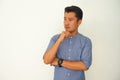 Portrait of a blue shirt young Asian deep in thought and beard guy standing confidently with his arms crossed against a white wall Royalty Free Stock Photo