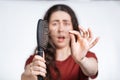Portrait in a blur, a screaming brunette woman holds a comb in front of her, clearing it from a pile of fallen hair.