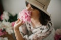 Portrait of boho girl smelling peony at pink and white peonies on rustic wooden floor. Stylish hipster woman in bohemian dress