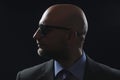 Portrait of a bold male man in dark suit and dark glasses. Bodyguard at work. Dark dramatic background