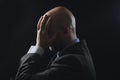 Portrait of a bold male man in dark suit hands at head, Pain concept. Bodyguard at work. Dark dramatic background