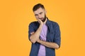 Portrait of bored Caucasian guy leaning on palm and looking at camera on orange studio background