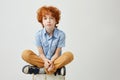 Portrait of bored little kid with red hair and freckles sitting on box with unhappy expression, being tired of waiting