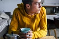 Portrait of bored serious teenager male having breakfast at home alone looking outside - young boy with yellow sweater drink a Royalty Free Stock Photo