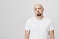 Portrait of bored and tired bald man with beard looking aside with gloomy expression, standing over gray background. Guy Royalty Free Stock Photo