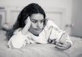 Portrait of a bored, unhappy and tired pretty young girl using mobile phone in bed Royalty Free Stock Photo