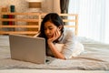 Portrait of bored young Asian girl lying down on bed while working from home in bedroom. Female freelancer working on Royalty Free Stock Photo