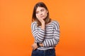 Portrait of bored young woman with brown hair in long sleeve striped shirt. indoor studio shot isolated on orange background Royalty Free Stock Photo