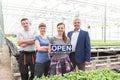 Portrait of botanist team standing with open sign in greenhouse