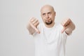 Portrait of bothered annoyed bald caucasian bearded man showing thumbs down, giving negative opinion while rolling eyes