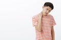 Portrait of bothered uneasy young asian man in striped t-shirt unwilling to do something rubbing neck tilting head and