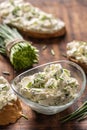 Portrait of a bowl of homemade cream cheese spread with chopped chives surrounded by bread slices with spread and a