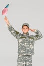 portrait of boy in camouflage clothing saluting while holding american flagpole in hand Royalty Free Stock Photo