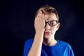 A portrait of a boy with eyeglasses close one eye with palm to chech vision in front of dark background. Children, ophthalmology