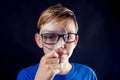 A portrait of a boy with eyeglasses looks through a magnifying glass in front of dark background. Children and education concept Royalty Free Stock Photo