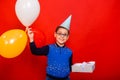 Portrait of a boy in a festive hat with colorful balloons and a box with a bow wrapped in silver paper. Royalty Free Stock Photo