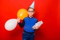 Portrait of a boy in a festive hat with colorful balloons and a box with a bow wrapped in silver paper. Royalty Free Stock Photo