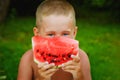 Portrait of a boy holding a slice of watermelon in front of his face on a green background of nature. A child eats a slice of Royalty Free Stock Photo