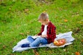 Portrait of a boy in a red plaid shirt at a picnic in the park with red apples. The child is sitting on a blanket and reading a