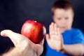 A portrait of a boy refuses an apple in front of dark background. Children and food concept