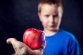 A portrait of a boy refuses an apple in front of dark background. Children and food concept