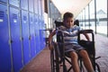 Portrait of boy sitting on wheelchair by lockers in corridor Royalty Free Stock Photo