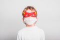 Portrait of boy in superhero mask with his mouth covered with a medical mask to protect himself from viral infections and diseases