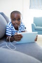 Portrait of boy using digital tablet while listening to headphones on sofa at home Royalty Free Stock Photo