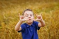 Portrait of a boy in a wheat field. The child holds a spikelet of wheat in his teeth and shows a thumbs-up with both hands