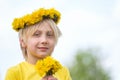 Portrait of boy with white hair wreath of flowers holds bouquet of dandelions looks at the camera and smiles