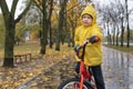 Portrait of boy in yellow raincoat on bicycle on autumn park background. Child riding bicycle in the rain