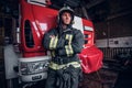 Young fireman wearing protective uniform standing next to a fire engine in a garage of a fire department Royalty Free Stock Photo