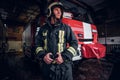 Young fireman wearing protective uniform standing next to a fire engine in a garage of a fire department Royalty Free Stock Photo