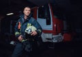 Young fireman wearing protective uniform standing next to a fire engine in a garage of a fire department Royalty Free Stock Photo