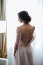 Portrait of the bride with open dress from the back on the window background. Beautiful neckline on the dress with sexy Royalty Free Stock Photo