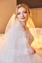 Portrait of a bride sitting in a chic white wedding dress on the bed and preparing for the wedding ceremony