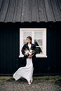 Portrait of a bride in a white silk wedding dress and a black coat with a bride`s bouquet in her hands. Black wooden Royalty Free Stock Photo