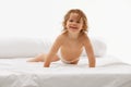 portrait of bright-eyed toddler, girl with playful smile crawling on soft and comfortable white bed against white Royalty Free Stock Photo