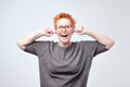 Portrait of bright mature caucasain woman with red hair covering ears with hands Royalty Free Stock Photo