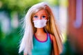 Portrait of brlonde Barbie doll with medical mask outdoors