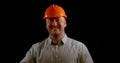 Portrait of a broadly smiling man on a black background in the studio, wearing an orange construction helmet and shirt Royalty Free Stock Photo