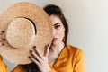 Portrait of brown-eyed girl covering face with straw hat. Beautiful lady in bright outfit looking at camera. Royalty Free Stock Photo