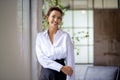 Portait of an attractive mid aged woman wearing white shirt and black pants and standing by the window Royalty Free Stock Photo