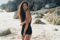 Portrait of brunette model in knitted sweater posing on the sandy beach, big stones and rock on background. Royalty Free Stock Photo