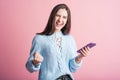 Portrait of a brunette on a pink background who uses a smartphone and shows the gesture of the winner. Royalty Free Stock Photo