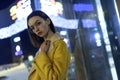Portrait of brunette posing in stylish jacket and glasses, lit by city center lights by night. Womenswear fashion. Blurred
